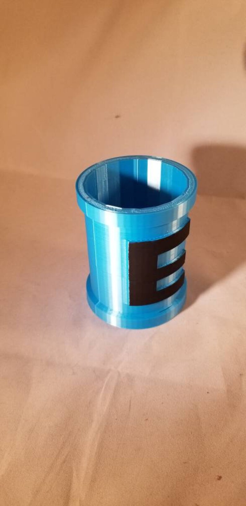 May include: A blue plastic container with a black stripe and the letter "E" printed on it.