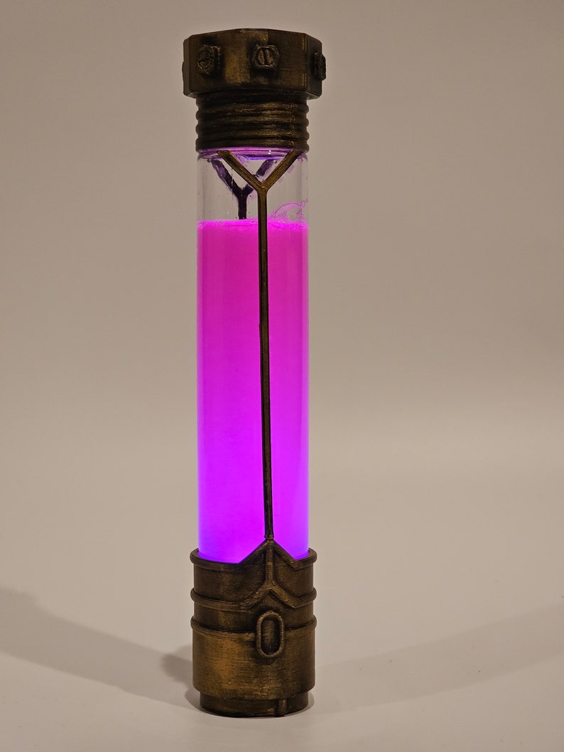 May include: A glass tube with a metallic cap and base, filled with a bright pink liquid. The tube has a decorative metal frame inside.