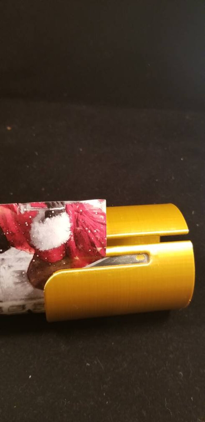 May include: A gold-colored wrapping paper dispenser with a red and white patterned wrapping paper partially inserted.