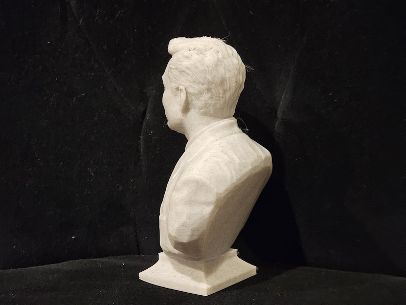 May include: White plaster bust sculpture of a person with short hair. The bust is on a white base.