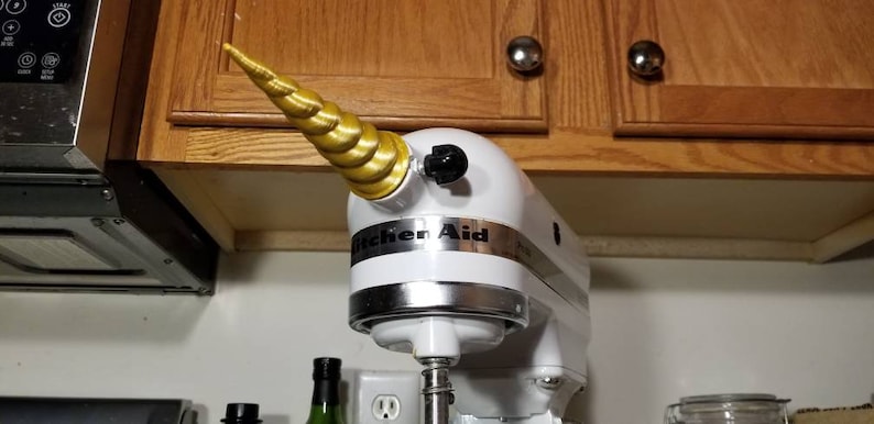 May include: A white KitchenAid stand mixer with a gold unicorn horn attached to the top. The horn is made of a spiral design.
