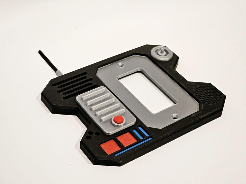 May include: A black and silver 3D printed device with a rectangular screen, a red button, and a silver button panel. The device has a black antenna and a small, round, gray knob on the top.