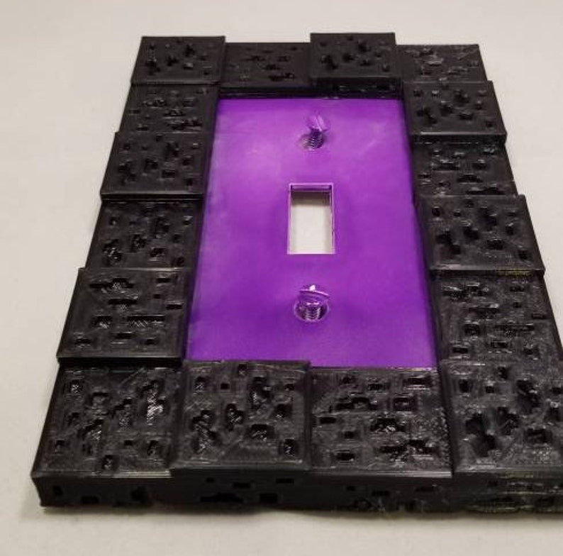 May include: A decorative light switch cover with a purple center and a black, textured border. The cover has a rectangular opening for the switch and two screws for mounting. The border has a unique, geometric design.