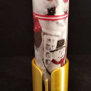 May include: A gold metal wrapping paper holder with a slot for cutting wrapping paper. The holder is designed to hold a roll of wrapping paper upright.