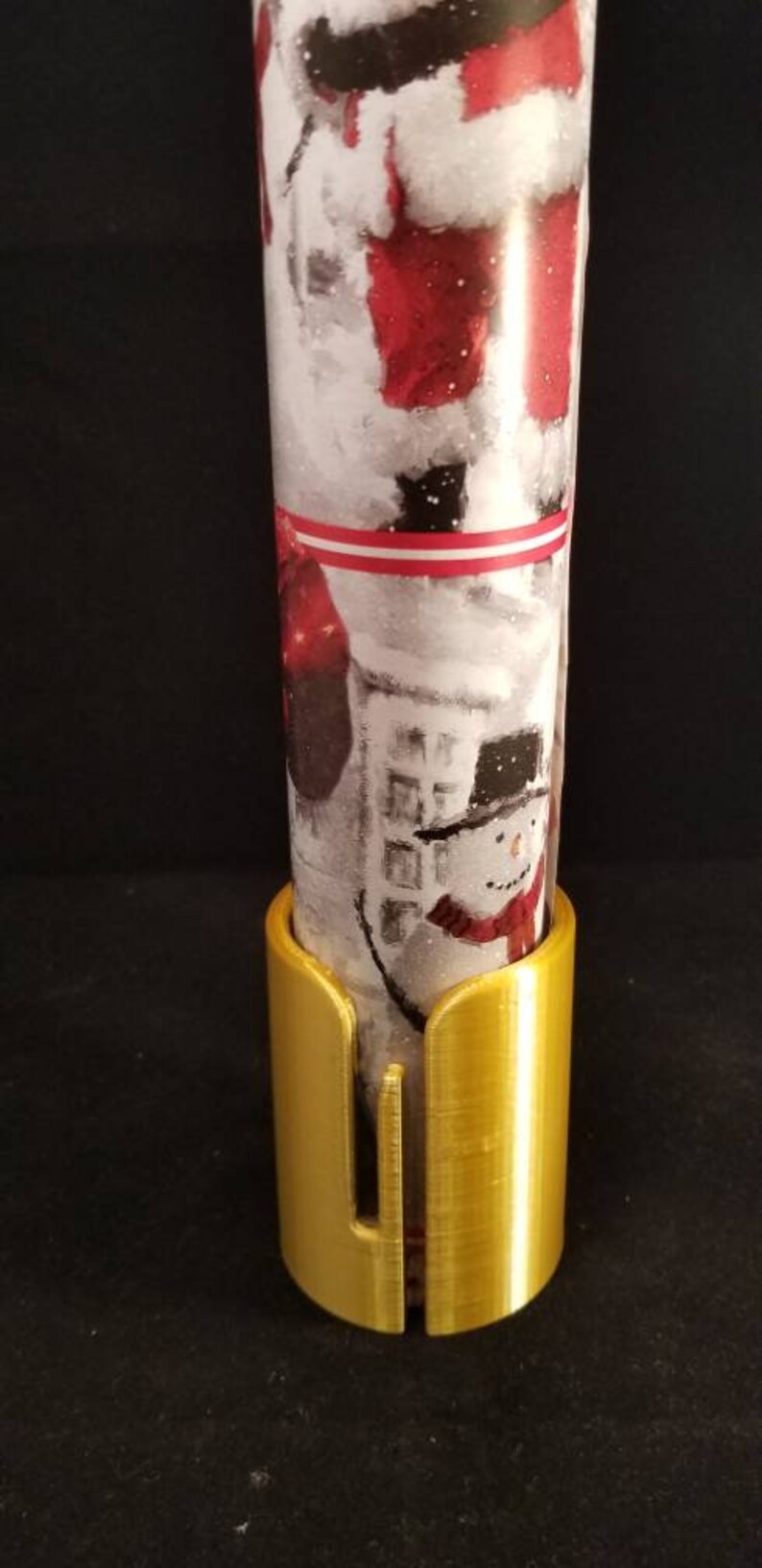 May include: A gold metal wrapping paper holder with a slot for cutting wrapping paper. The holder is designed to hold a roll of wrapping paper upright.