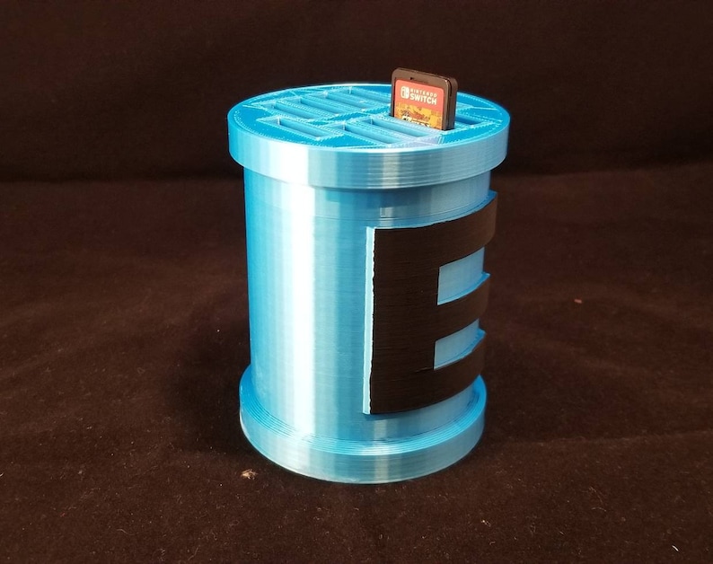 May include: A light blue 3D printed game cartridge holder with a black stripe design and a slot for a Nintendo Switch game cartridge. The holder is designed to hold multiple game cartridges.