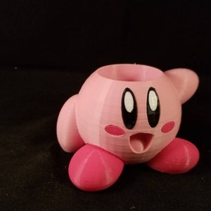 May include: A pink 3D printed planter shaped like the video game character Kirby. The planter has a hole in the top for planting.