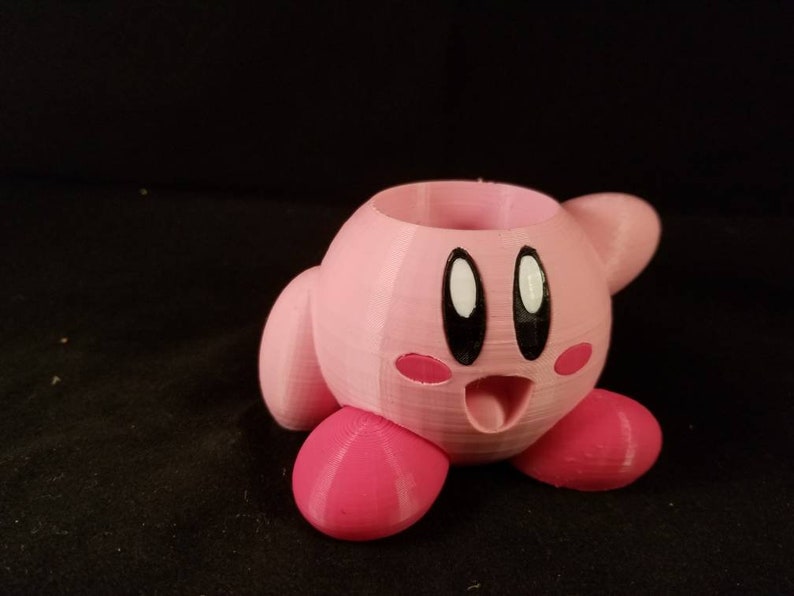 May include: A pink 3D printed planter shaped like the video game character Kirby. The planter has a hole in the top for planting.