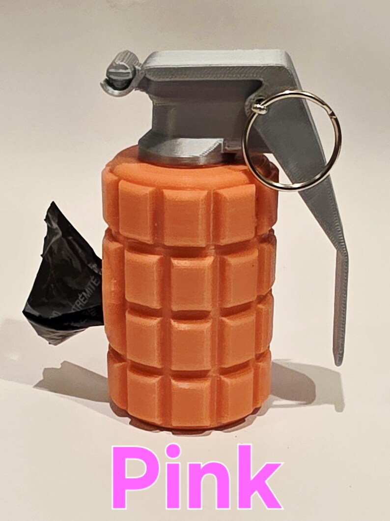 May include: A pink grenade with a gray top and pull ring. The body of the grenade is a textured, rectangular design. A black object is attached to the side. The word "Pink" is written in pink at the bottom.