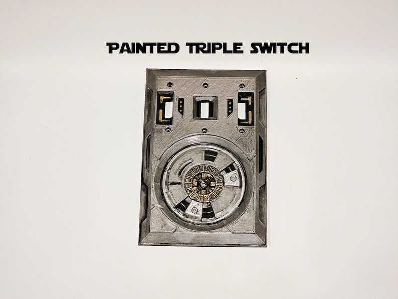 Pode incluir: Uma placa de interruptor triplo pintada em prata com um bot&atilde;o redondo, detalhado, prateado e dourado no centro. O texto "PAINTED TRIPLE SWITCH" est&aacute; impresso acima da placa.