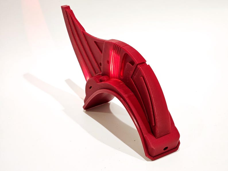 Op de afbeelding: Een rood kunststof onderdeel met een gebogen vorm en ingewikkelde details. Het onderdeel heeft een gladde, glanzende afwerking en lijkt een onderdeel te zijn van een groter apparaat of machine.