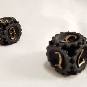May include: Two black dice with gold numbers. The dice have a textured surface and are shaped like gears.