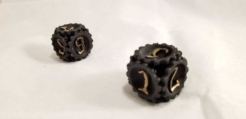 May include: Two black dice with gold numbers. The dice have a textured surface and are shaped like gears.