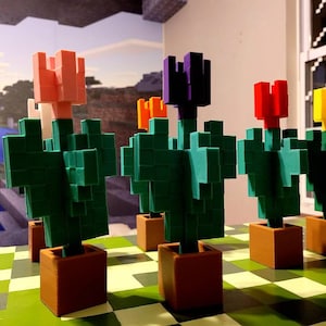 May include: Five 3D printed Minecraft flower pots with different colored flowers. The flowers are pink, purple, red, yellow, and orange. The pots are brown and the flowers are on a green and brown checkered surface.