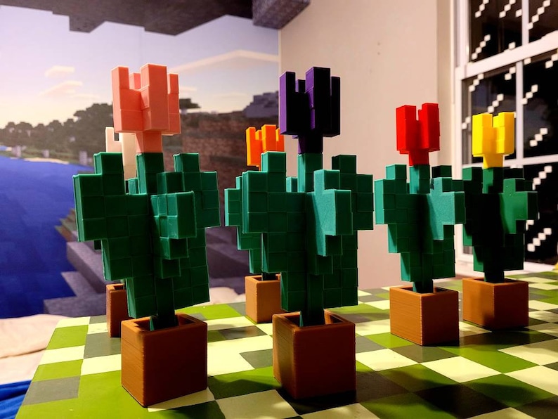 May include: Five 3D printed Minecraft flower pots with different colored flowers. The flowers are pink, purple, red, yellow, and orange. The pots are brown and the flowers are on a green and brown checkered surface.