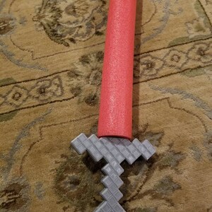 Op de afbeelding: Een rode schuimrubberen zwembadnoodle met een grijs plastic Minecraft-zwaard aan het uiteinde.