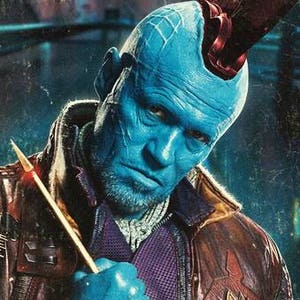 May include: A blue-skinned character with a red mohawk and a brown leather jacket holds a gold-colored weapon. The character has a serious expression on their face.