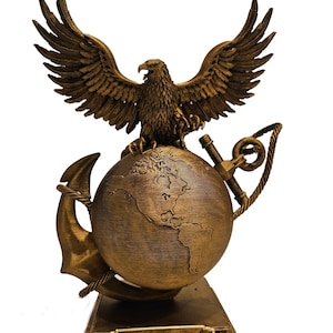 May include: A bronze-colored sculpture featuring an eagle with outstretched wings atop a globe, an anchor, and rope. The base has the name "Smith" and military insignia. The sculpture is a decorative item.