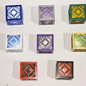 K&ouml;nnte beinhalten: Neun dekorative Boxen mit geometrischen Mustern. Die Boxen sind in verschiedenen Farben, darunter Blau, Wei&szlig;, Lila, Gr&uuml;n, Gold, Rot und Schwarz.