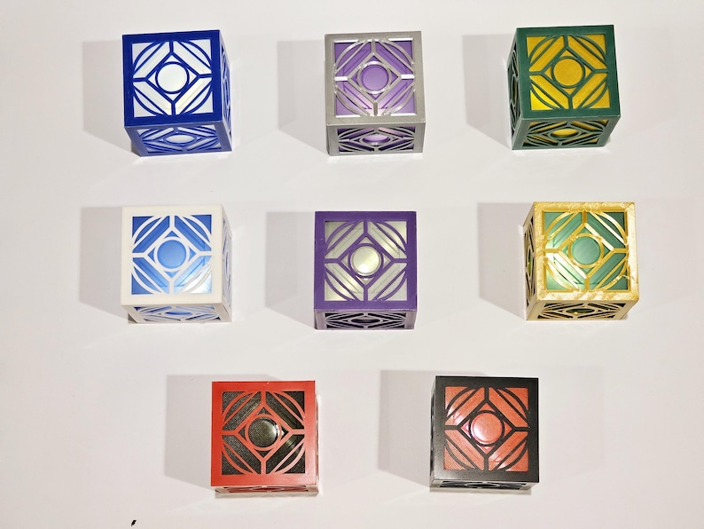 K&ouml;nnte beinhalten: Neun dekorative Boxen mit geometrischen Mustern. Die Boxen sind in verschiedenen Farben, darunter Blau, Wei&szlig;, Lila, Gr&uuml;n, Gold, Rot und Schwarz.