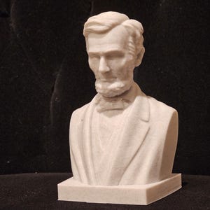 May include: A white bust sculpture of Abraham Lincoln, the 16th President of the United States. The bust is on a white base.