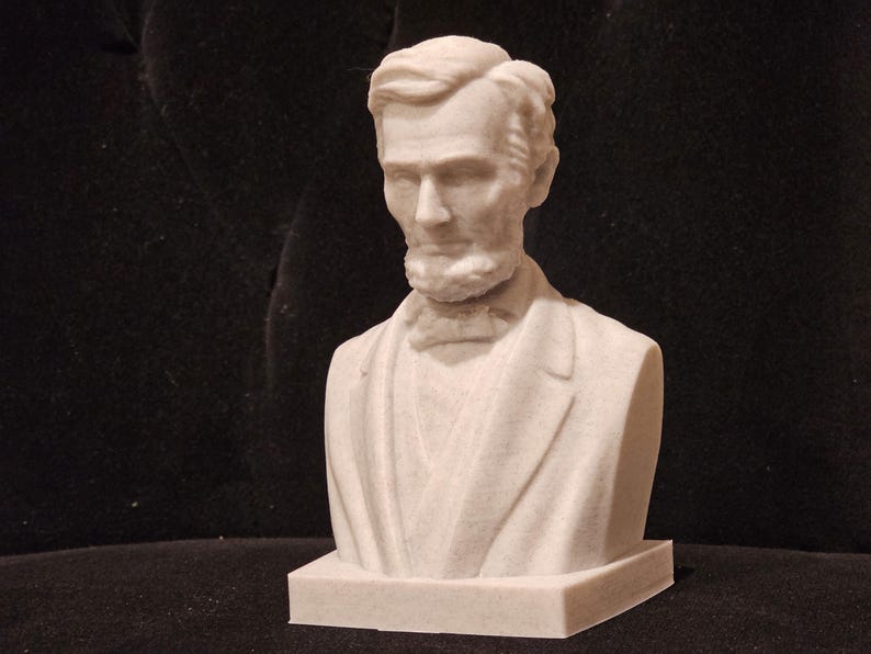 May include: A white bust sculpture of Abraham Lincoln, the 16th President of the United States. The bust is on a white base.