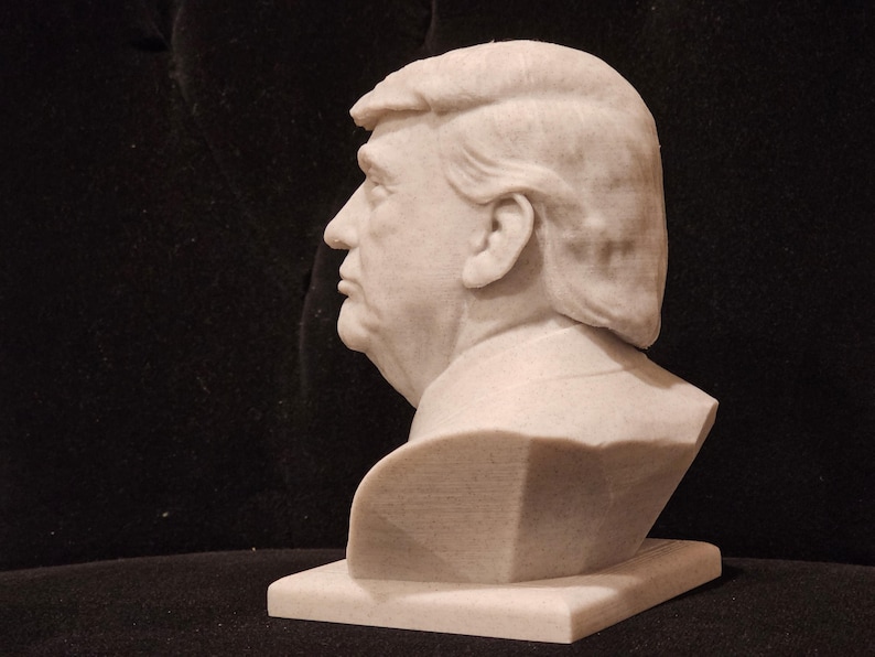 May include: A white marble bust sculpture of a person with short, wavy hair. The bust is on a white rectangular base.