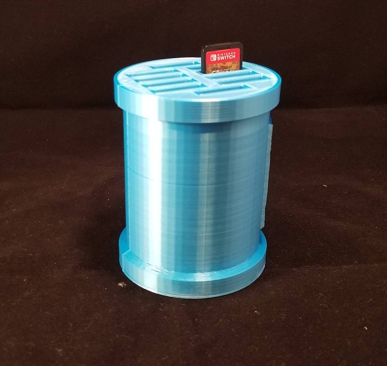 May include: A light blue plastic storage container with a gridded top for holding Nintendo Switch game cartridges. A game cartridge is inserted into the top of the container.