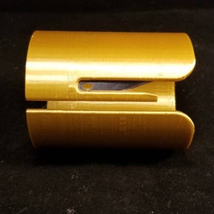 May include: A gold-colored plastic paper cutter with a black blade. The cutter is designed to be used with one hand.