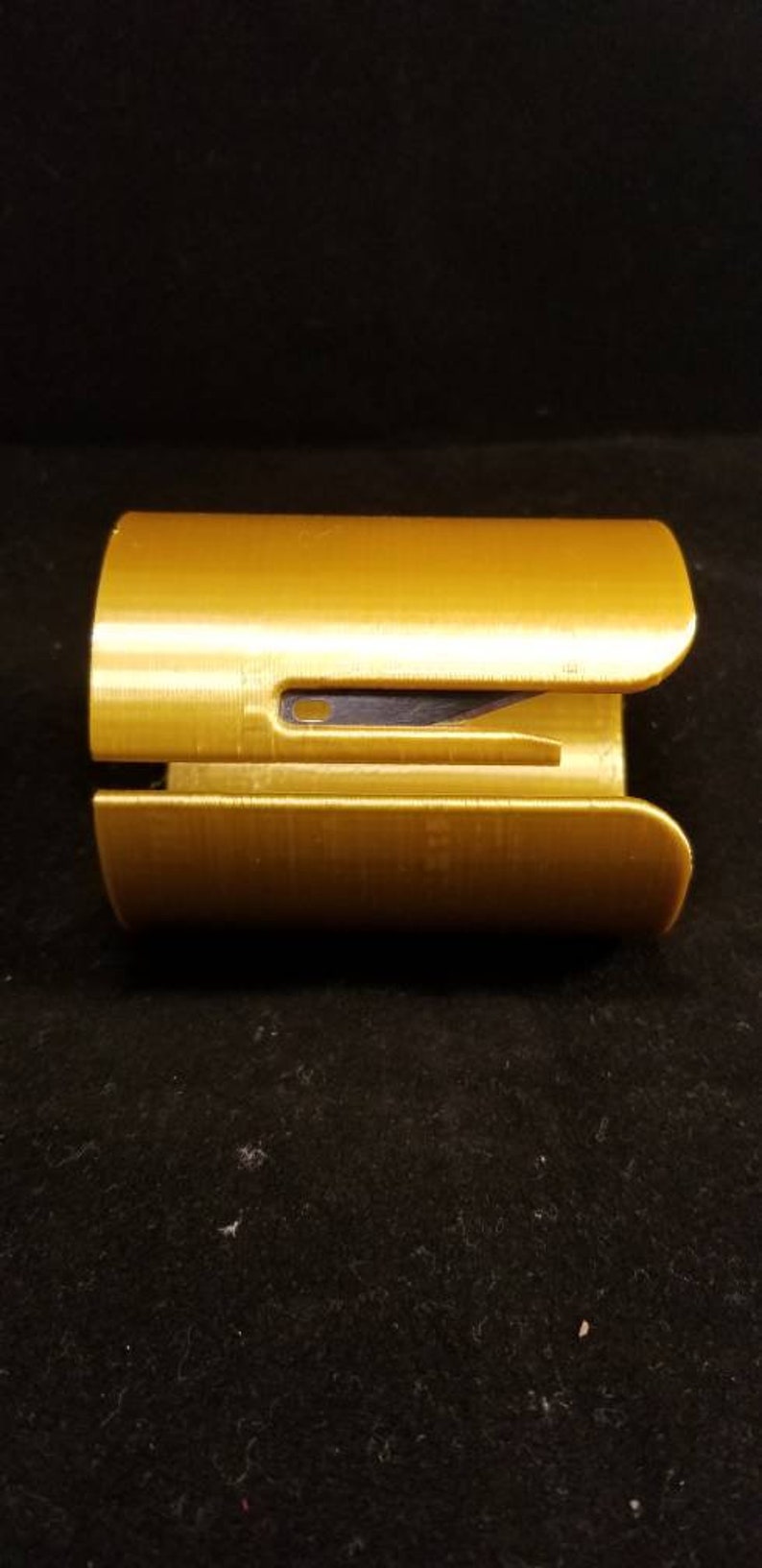 May include: A gold-colored plastic paper cutter with a black blade. The cutter is designed to be used with one hand.