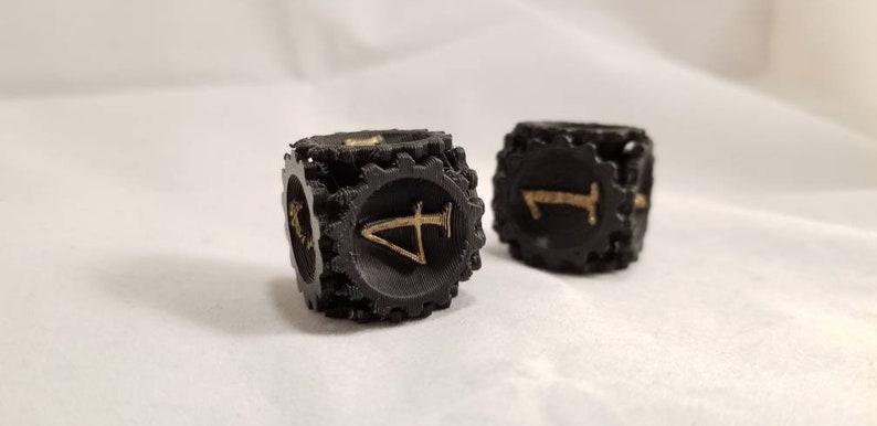 May include: Two black dice with gold numbers. The dice have a gear-like design around the edges.