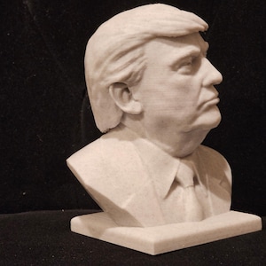 May include: A white bust sculpture of a person with short, styled hair. The sculpture is on a white base.