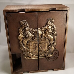 May include: A wooden box with two doors, featuring a gold-colored crest with two lions and a shield. The box has a brown stain finish and a decorative design on the front.