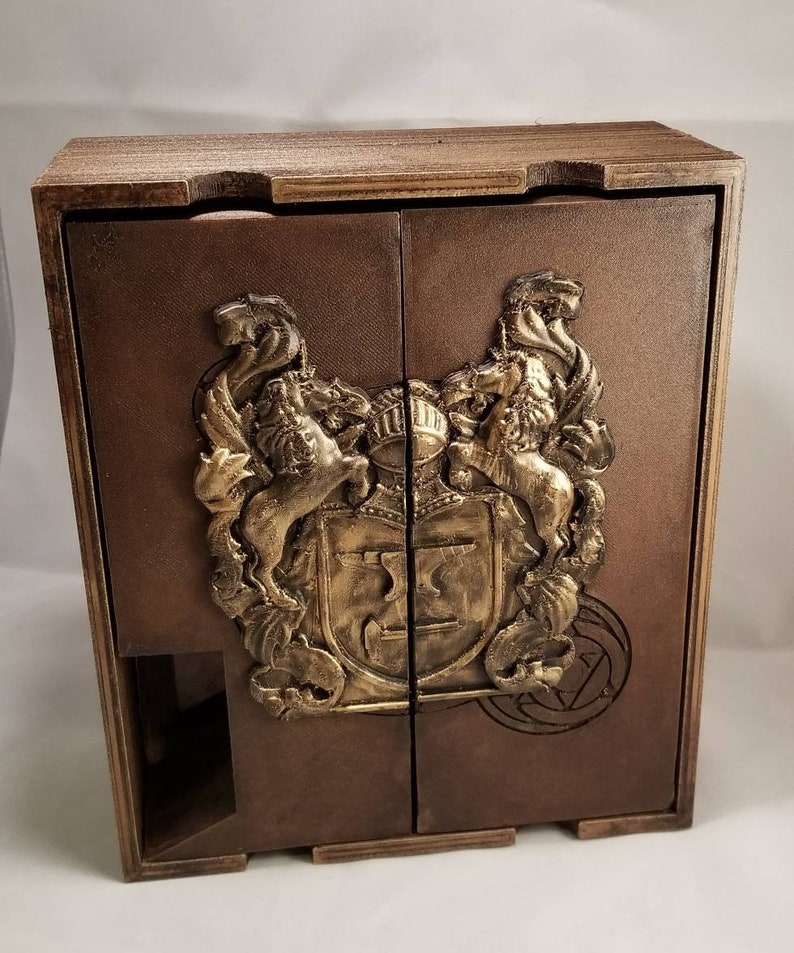 May include: A wooden box with two doors, featuring a gold-colored crest with two lions and a shield. The box has a brown stain finish and a decorative design on the front.