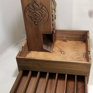 May include: A wooden dice tower with a dragon design and a pull-out drawer with compartments for dice. The tower is made of dark wood and has a brass accent.