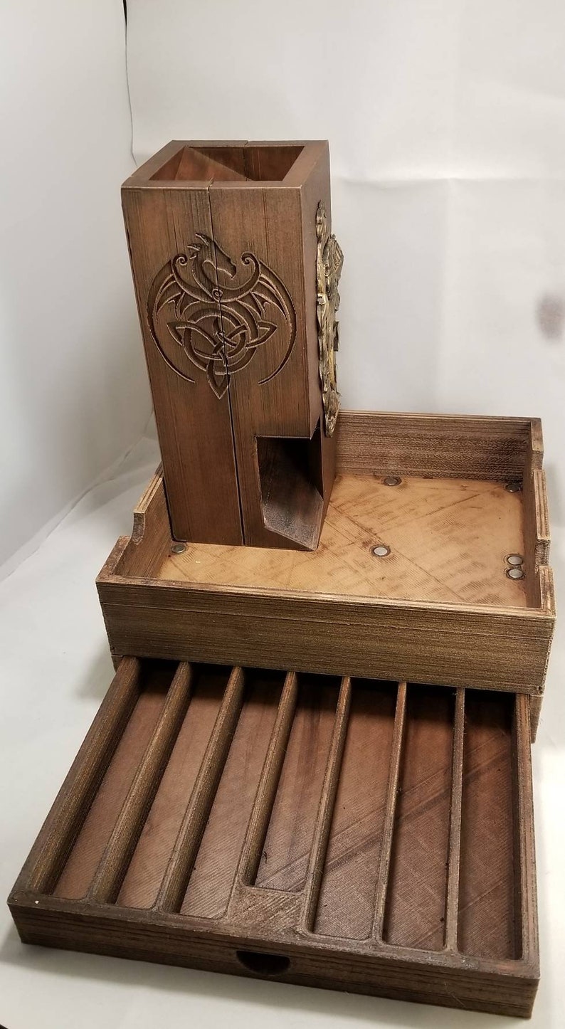 May include: A wooden dice tower with a dragon design and a pull-out drawer with compartments for dice. The tower is made of dark wood and has a brass accent.