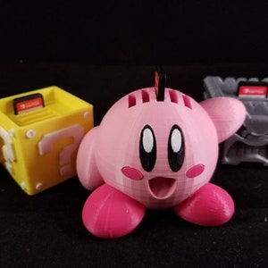 May include: Three 3D printed Nintendo Switch game card holders. One is a pink Kirby character, one is a yellow question block, and one is a gray block with a question mark.