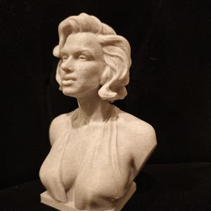 May include: A white bust sculpture of a woman with short, wavy hair. The sculpture is made of a textured material and depicts the woman with a classic, elegant pose.