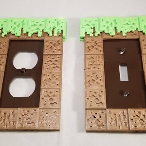 May include: Two 3D printed wall plates, one for a light switch and one for a double outlet, with a green grass block design on top and a brown dirt block design on the bottom.