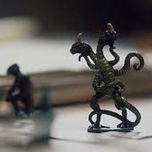 May include: A green, three-headed monster figurine with a long, curled tail. The monster has a textured, scaly surface and is standing on a white surface.