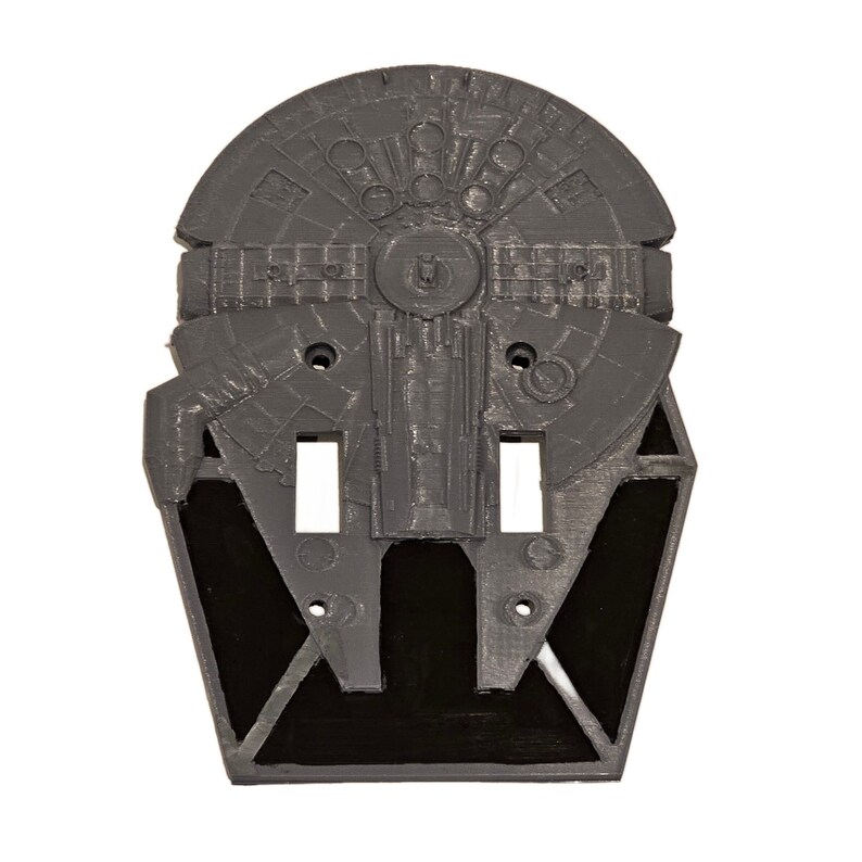 May include: A gray and black light switch cover featuring a 3D design of the Millennium Falcon from Star Wars.