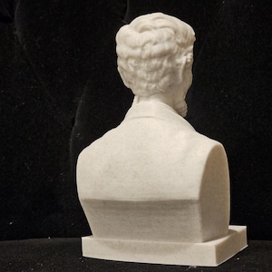 May include: White marble bust sculpture of a man with short hair, viewed from the back. The bust is on a white base.