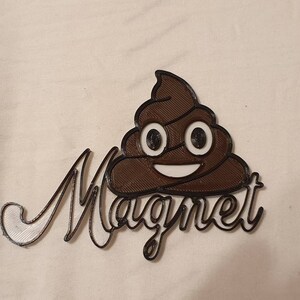 May include: A brown 3D printed poop emoji with a white smiling face and the word "Magnet" written in white 3D printed letters.