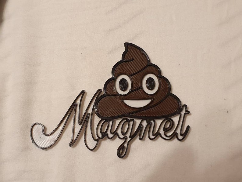 May include: A brown 3D printed poop emoji with a white smiling face and the word "Magnet" written in white 3D printed letters.