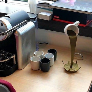 May include: A black and silver espresso machine with a drip tray and a cup holder. Four white ceramic mugs are on the counter, and a white ceramic cup is pouring a brown liquid into a gold-colored splash.