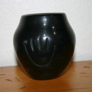 May include: A black ceramic vase with a hand-shaped design. The vase is smooth and has a glossy finish.