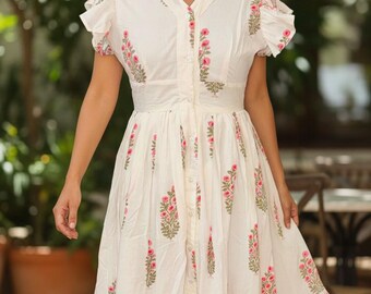 May include: White midi dress with a floral print in pink and green. The dress features short sleeves, a button-down front, and a fitted waist. The dress is made of a lightweight fabric and is suitable for warm weather.