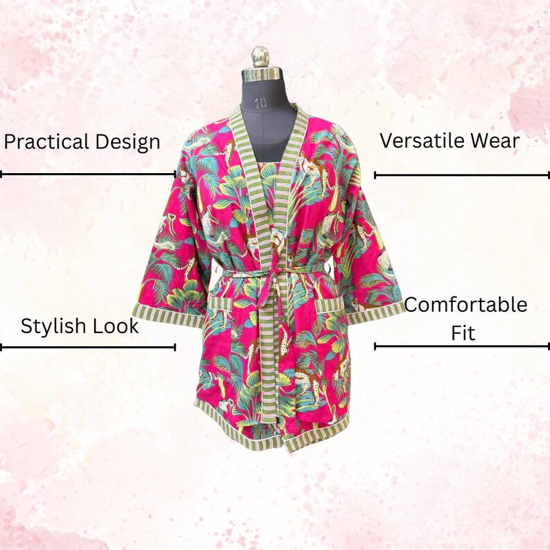 May include: A vibrant pink robe with a green and white striped trim and belt. The robe features a tropical print with green leaves and animal figures. The robe is displayed on a mannequin.