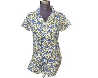 May include: A short-sleeved romper with a floral pattern. The romper features a white background with blue flowers and green leaves. It has a collared neckline and a button-down front. The garment is displayed on a mannequin.