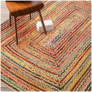 May include: A rectangular braided jute rug with a vibrant, multicolored striped pattern. The rug features shades of red, yellow, green, blue, and brown. A wooden chair and a stack of white books are partially visible on the rug.